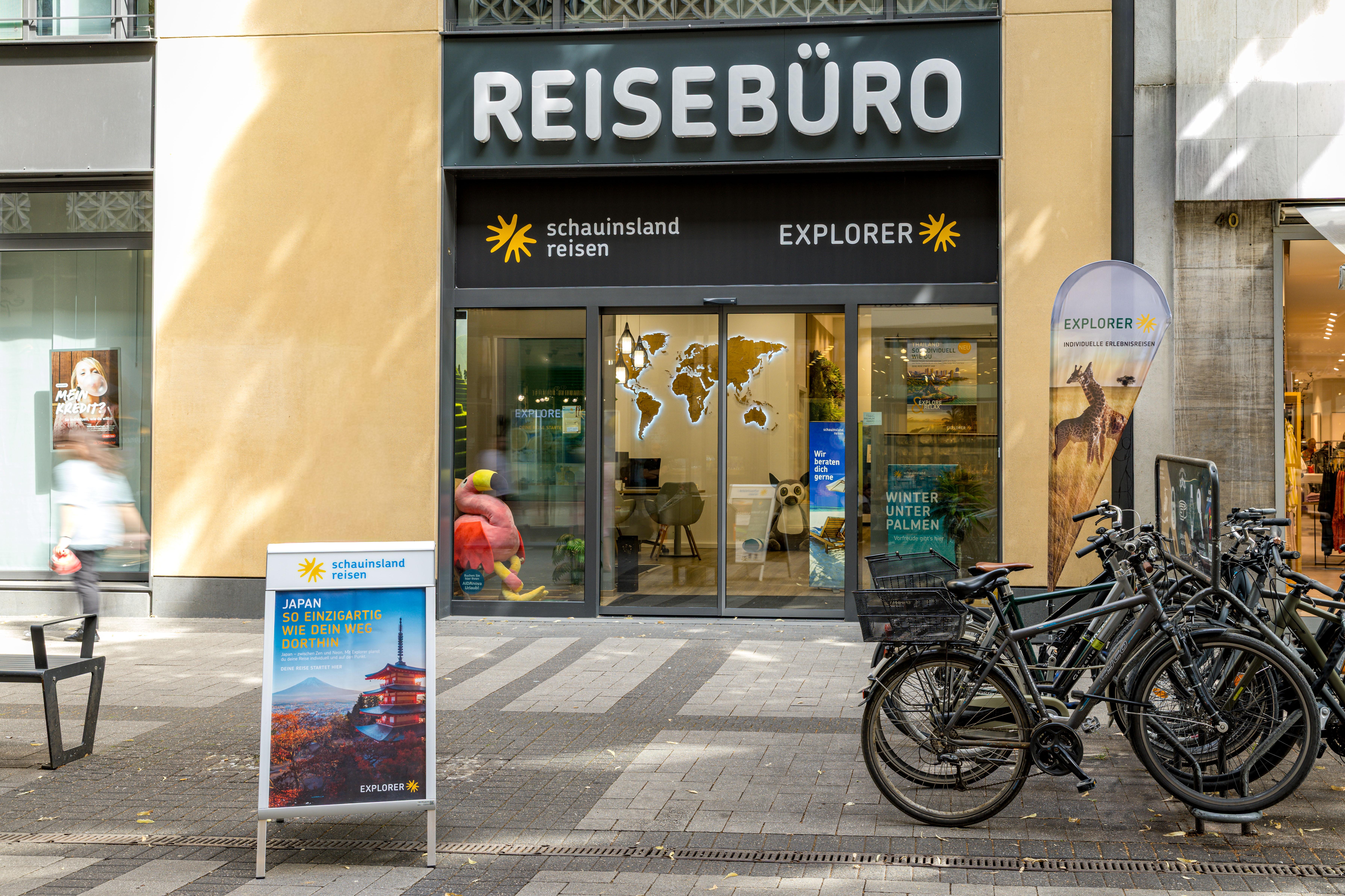 Ein modernes Reisebüro in der Stadt mit Werbetafeln, Sitzgelegenheiten und abgestellten Fahrrädern.