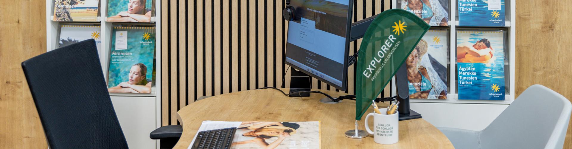 Moderner Reisebüroschalter mit Monitor, farbenfrohen Katalogen und Holzverkleidung im Hintergrund.