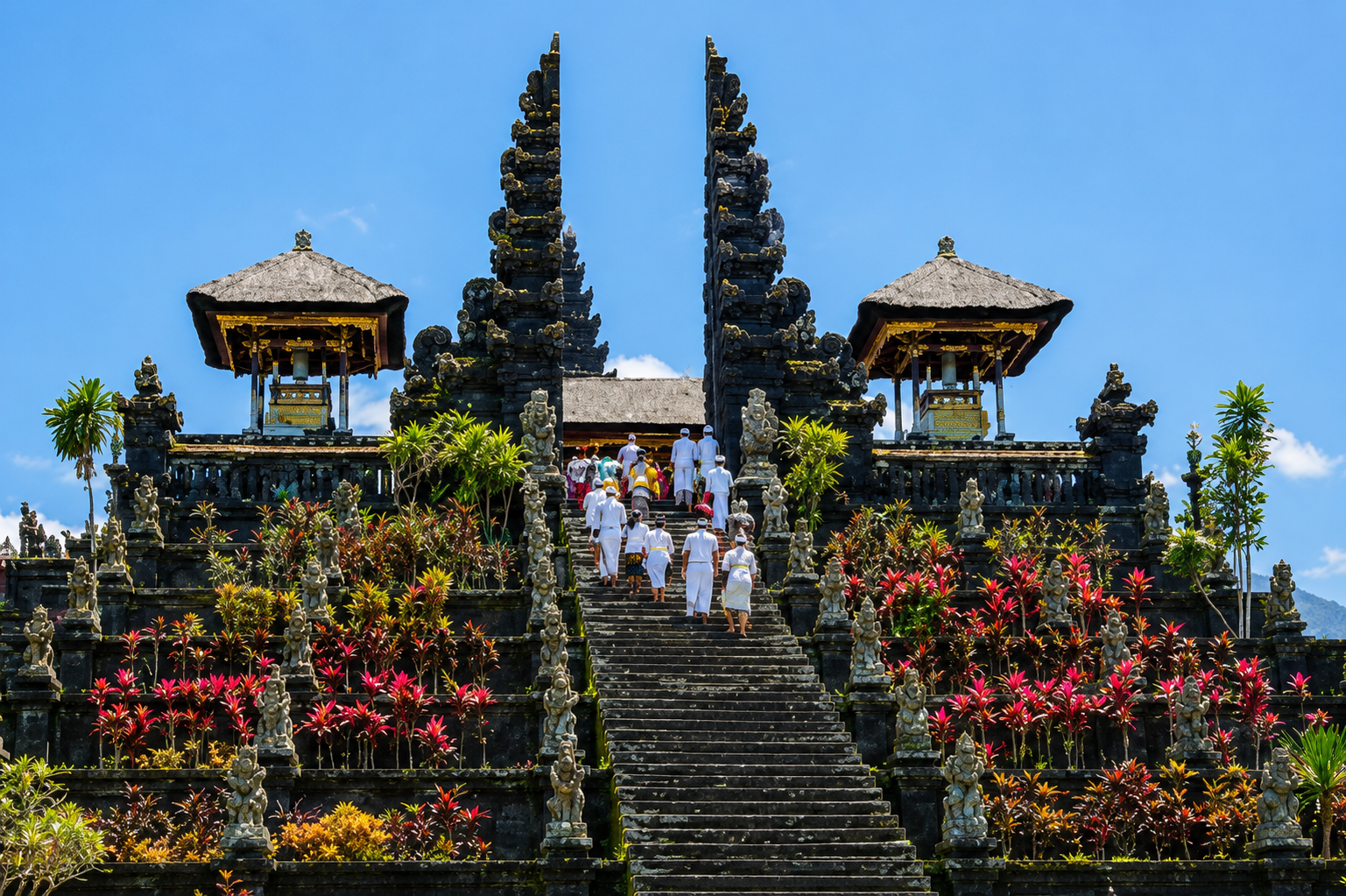Traditioneller balinesischer Tempel mit Treppen, schwarzen Steinreliefs und bunten Pflanzen.
