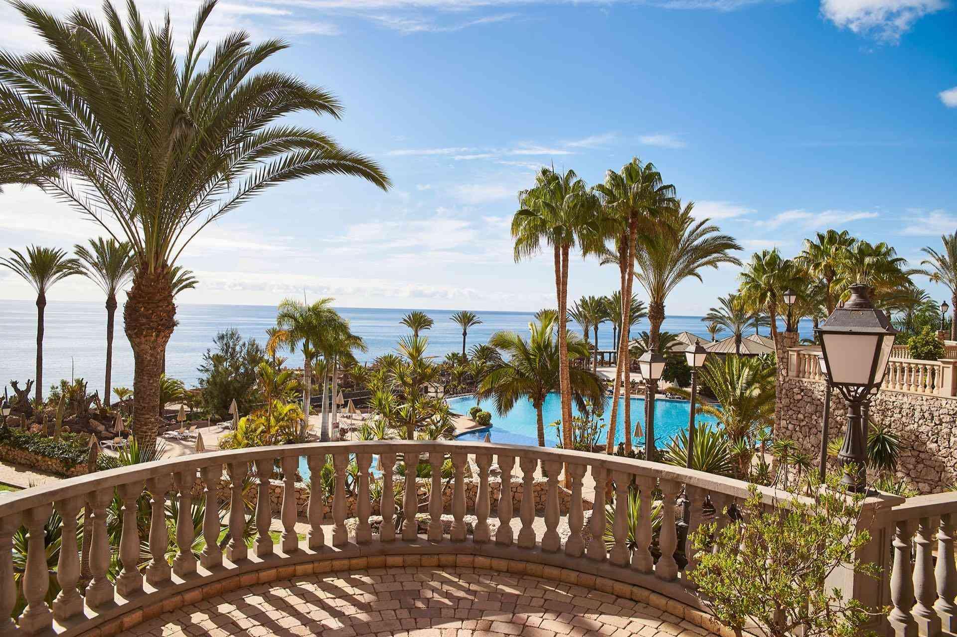 Luxuriöse Hotelanlage mit Palmen, großem Pool und Meerblick unter blauem Himmel.
