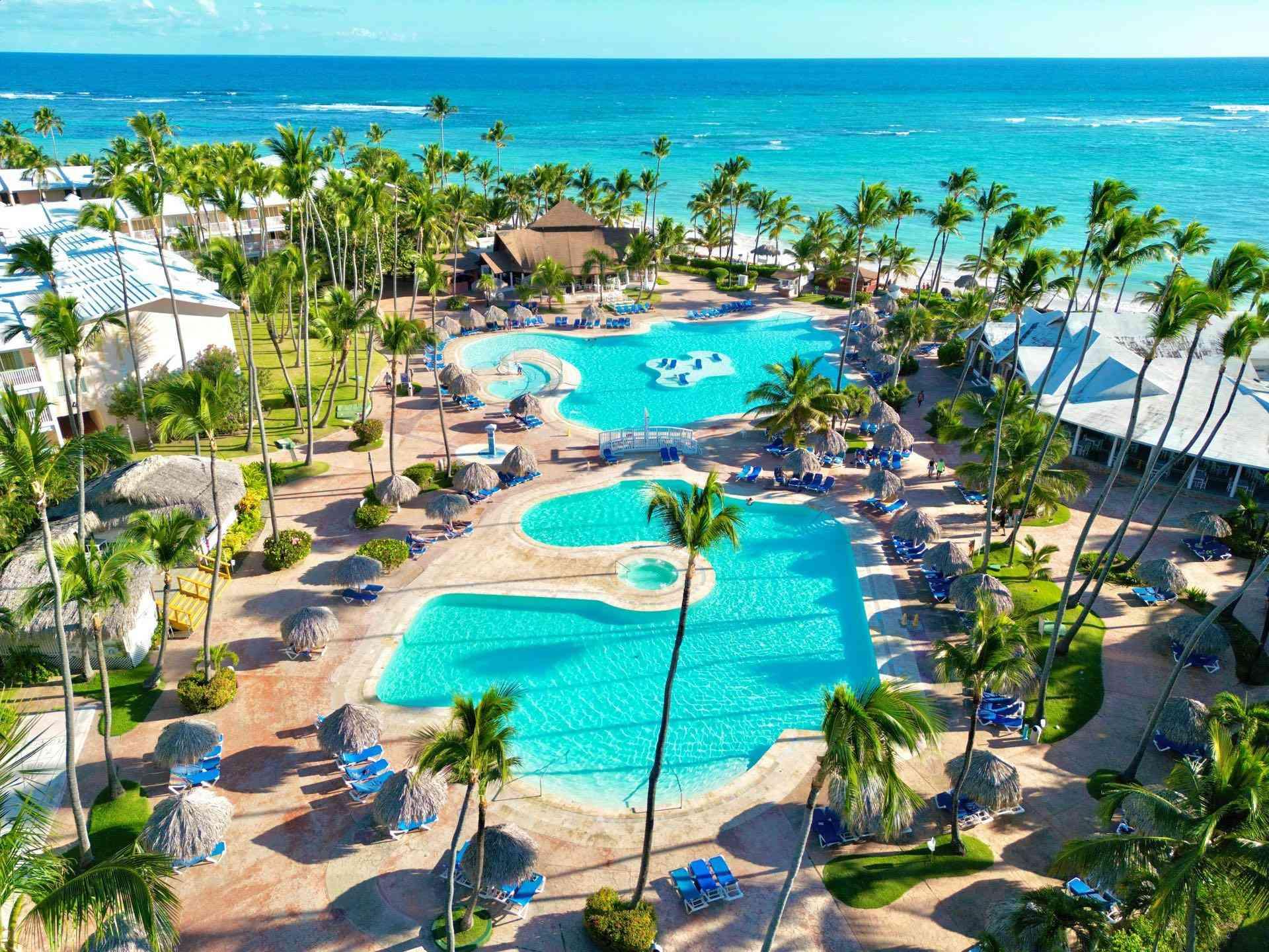 Großes Resort mit mehreren Swimmingpools, Palmen und Blick auf das türkisfarbene Meer am Strand.
