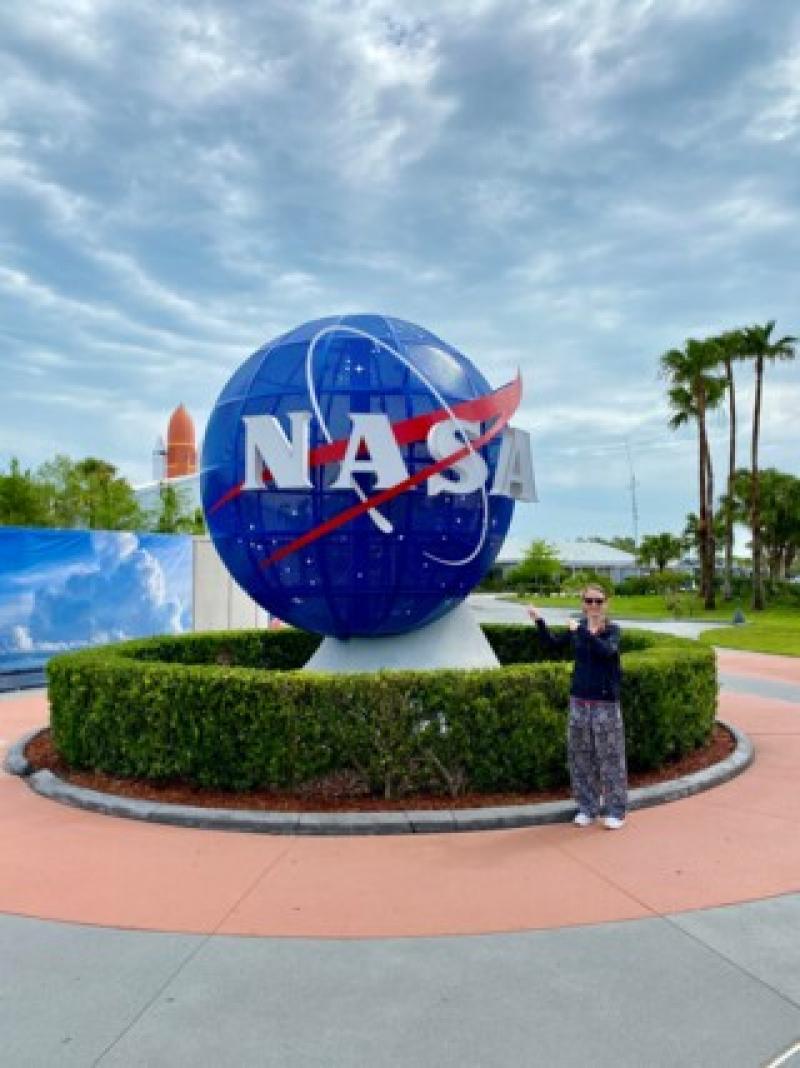 Gro&szlig;es blaues NASA-Logo vor B&uuml;schen, Palmen und bew&ouml;lktem Himmel am Urlaubsziel Weltraumzentrum.