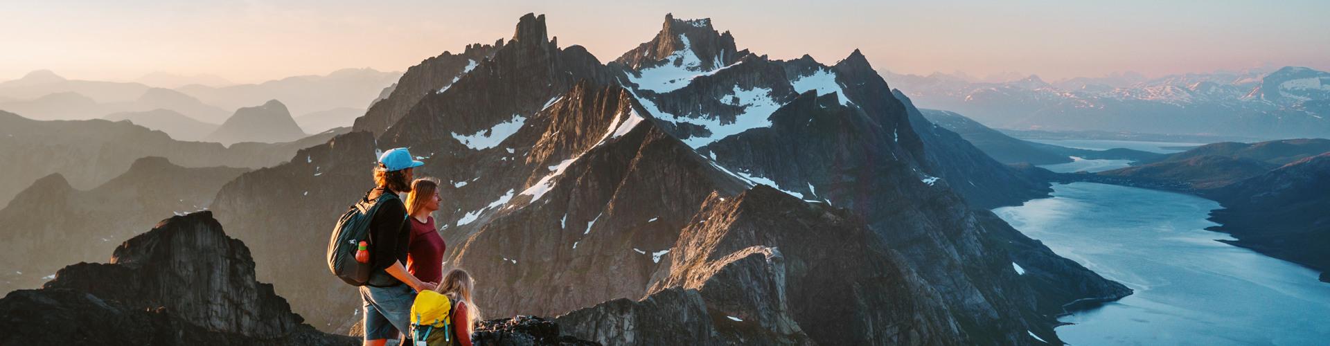Wanderer genießen den Panoramablick auf schneebedeckte Berge und einen tiefblauen See bei Sonnenuntergang.