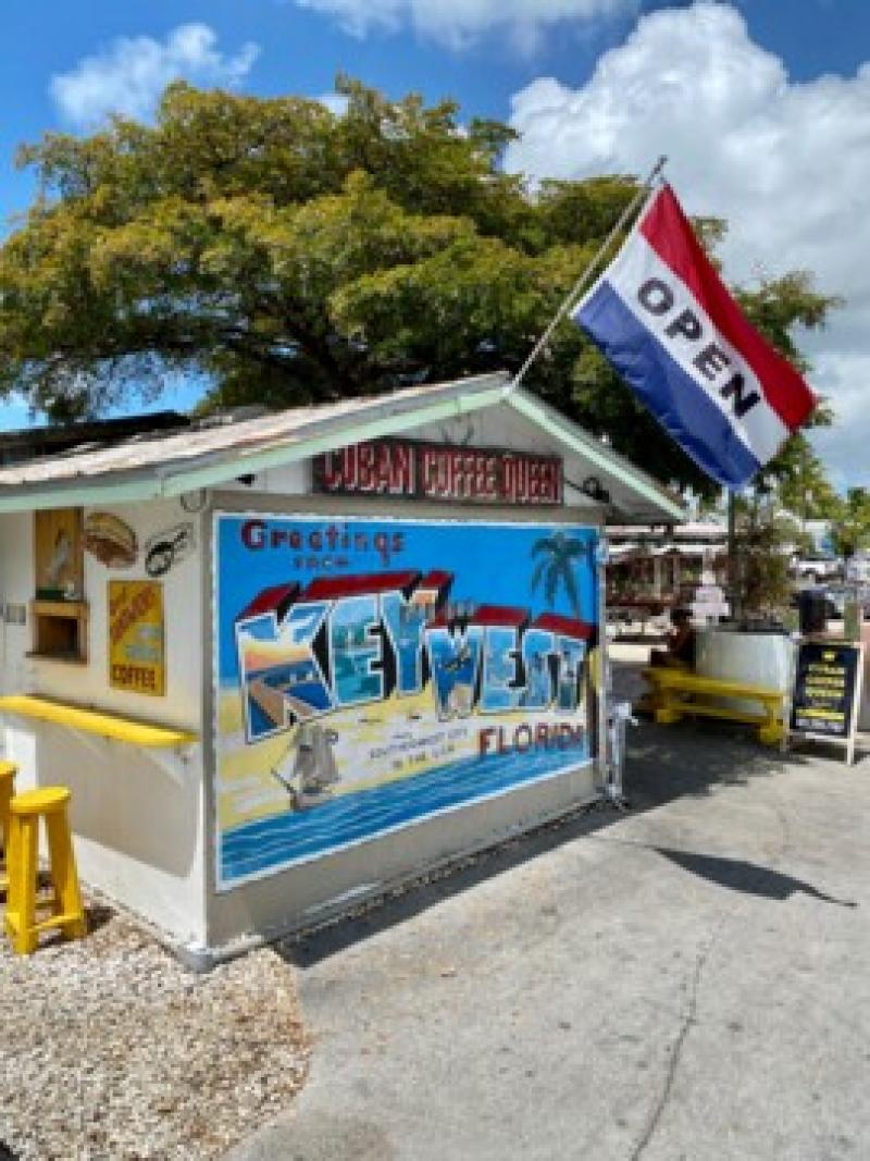 Kleiner Kaffeestand mit bunter Key West-Wandmalerei und offenem Flagge bei sonnigem Himmel.