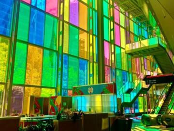 Bunte Glasfenster in einem hellen, modernen Hotel-Lobbybereich mit Treppe und Sitzplätzen.