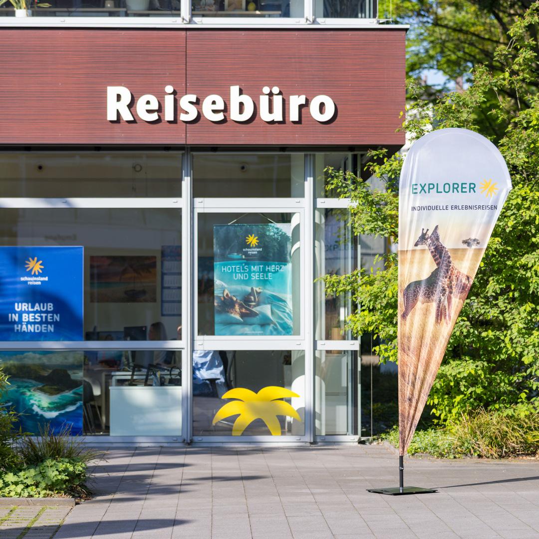 Modernes Reisebüro mit Werbeplakaten zu Urlaubsdestinationen und Safari-Themen, umgeben von Grün.
