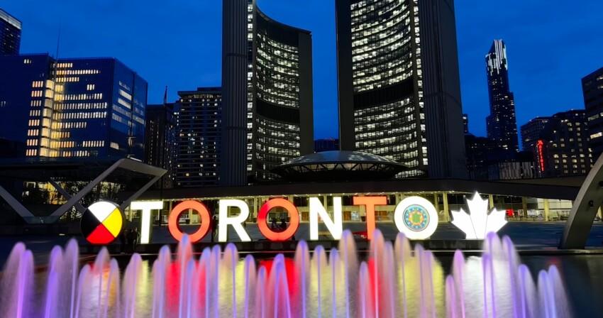 Bunte Wasserspiele vor beleuchteter Skyline mit Hotels im Zentrum von Toronto bei Abenddämmerung.