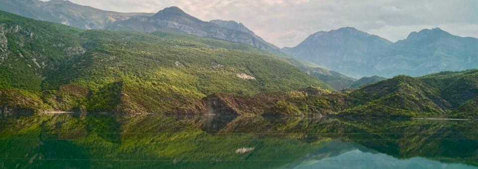 Berglandschaft mit grün bewachsenen Hügeln spiegelt sich klar in einem ruhigen See wider.