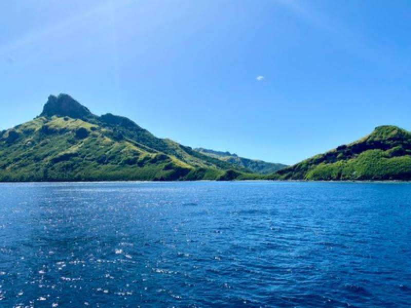 Klare blaue See vor gr&uuml;nen, bergigen Inseln unter hellem, wolkenlosem Himmel am Urlaubsziel.