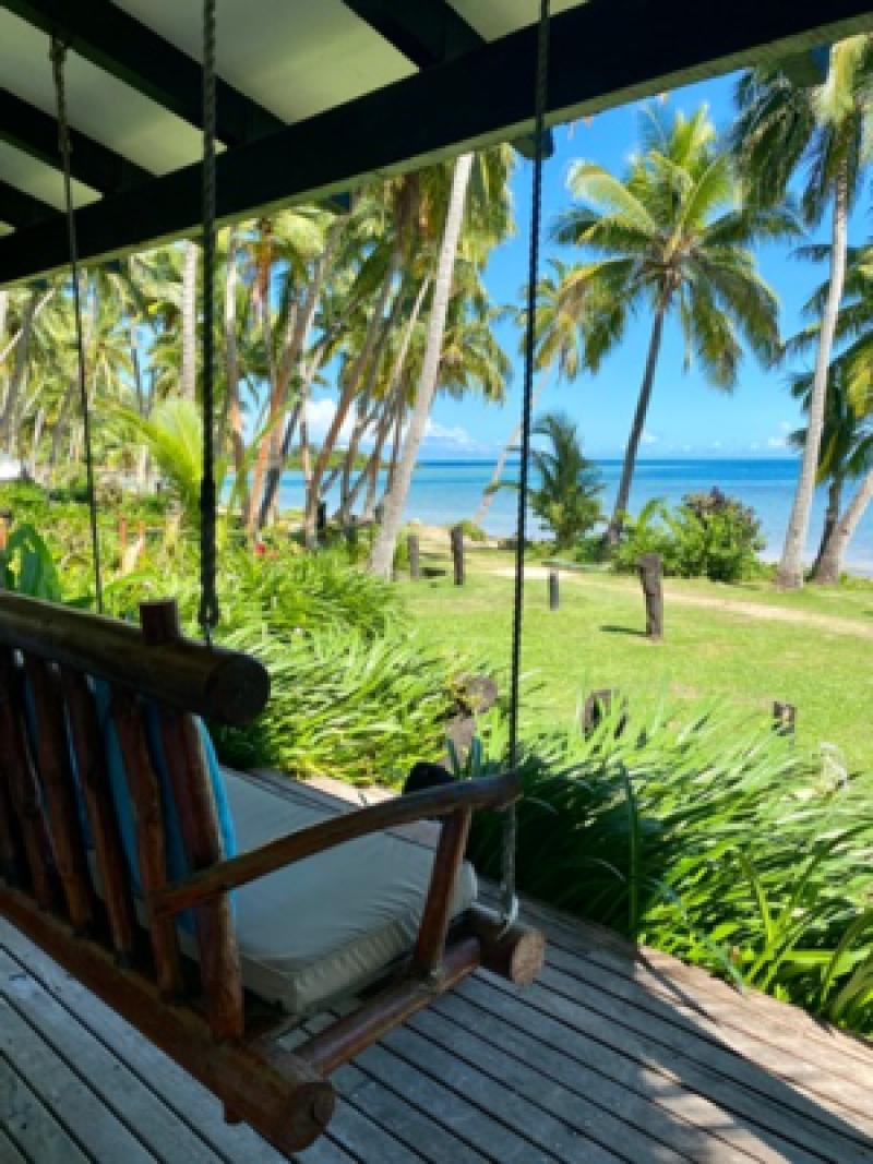 Veranda mit Schaukelstuhl, gr&uuml;ner Palmenlandschaft und sichtbar blauem Meer im sonnigen K&uuml;stenhotel.