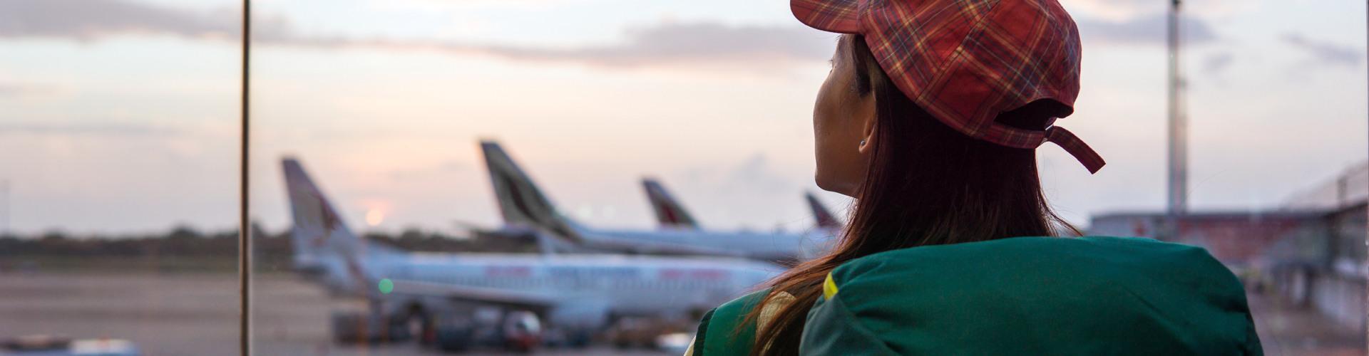 Eine Reisende beobachtet Flieger am Flughafen vor dem Abflug zu ihrem Urlaubsziel.