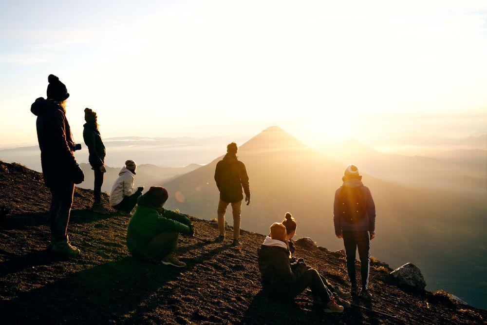 Touristen genießen den Sonnenaufgang auf einem Berggipfel mit weitem Blick auf Täler und Berge.