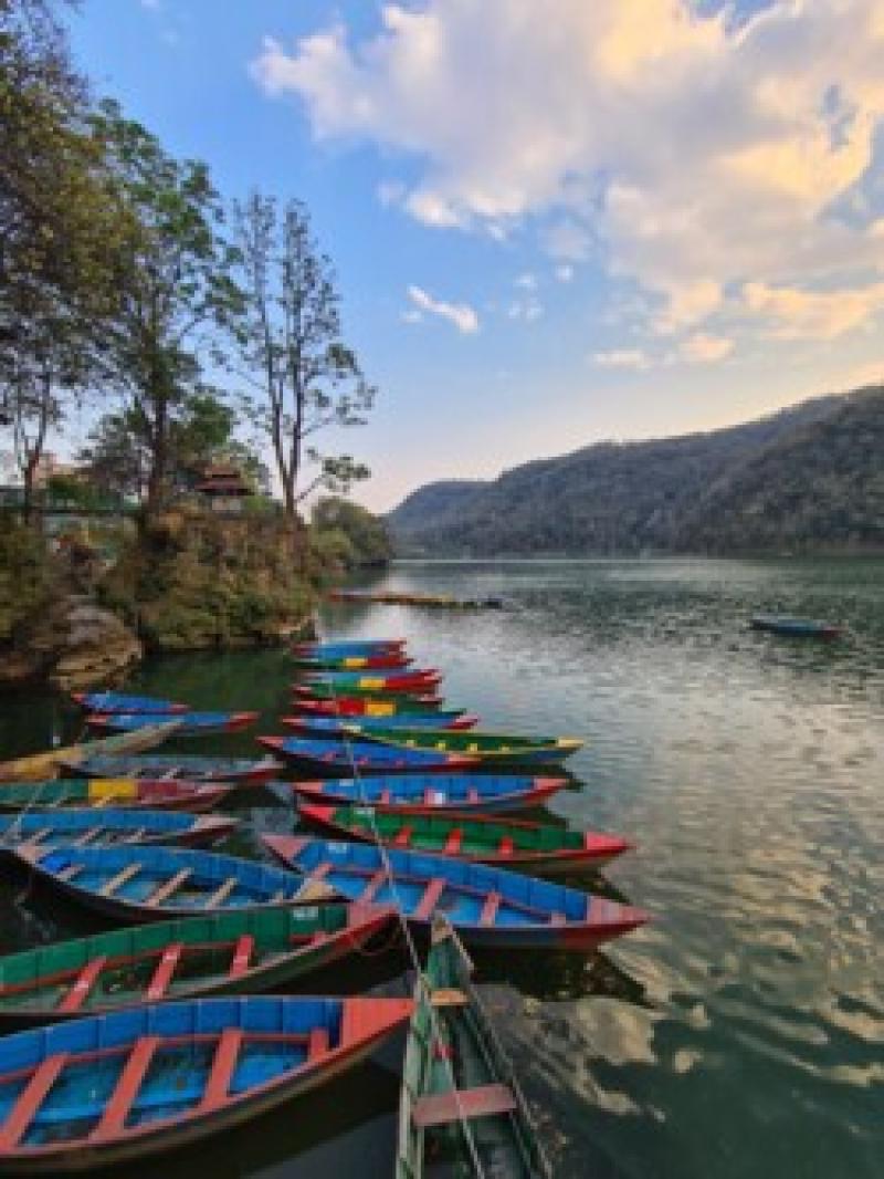Bunte Boote liegen an einem Seeufer, umgeben von gr&uuml;nen H&uuml;geln und blauem Himmel.