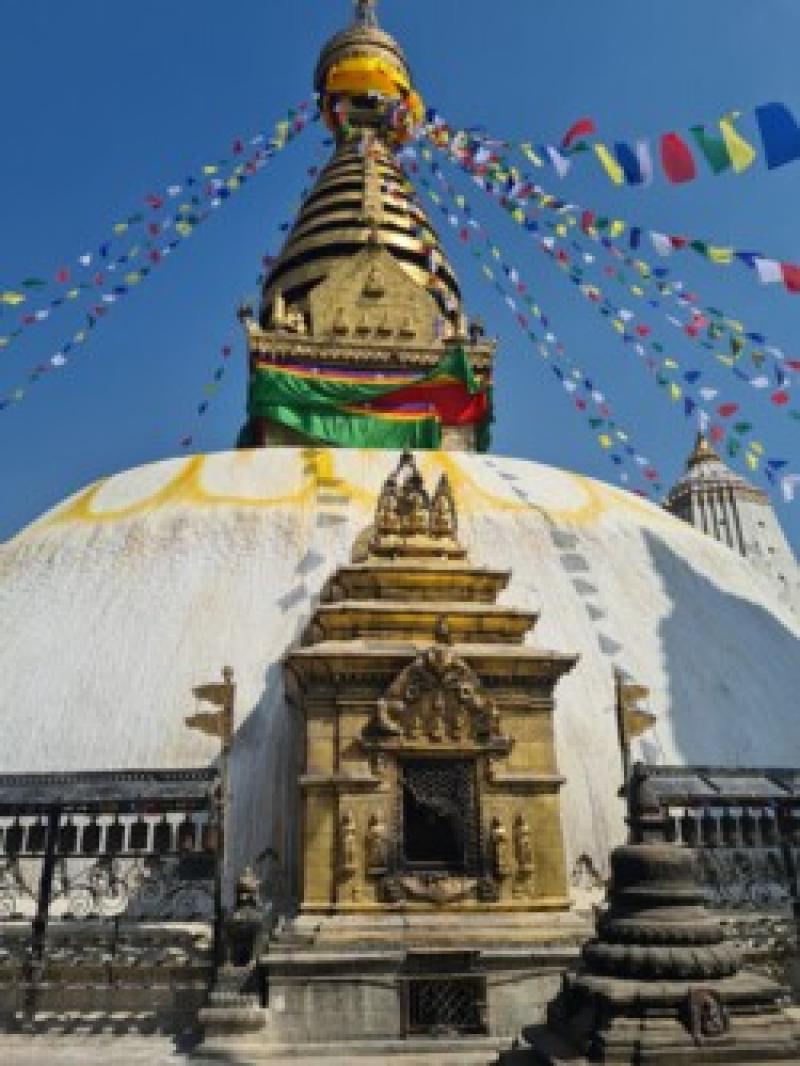 Ein wei&szlig;er Stupa mit vergoldetem Turm und bunten Gebetsfahnen vor klarem blauem Himmel.