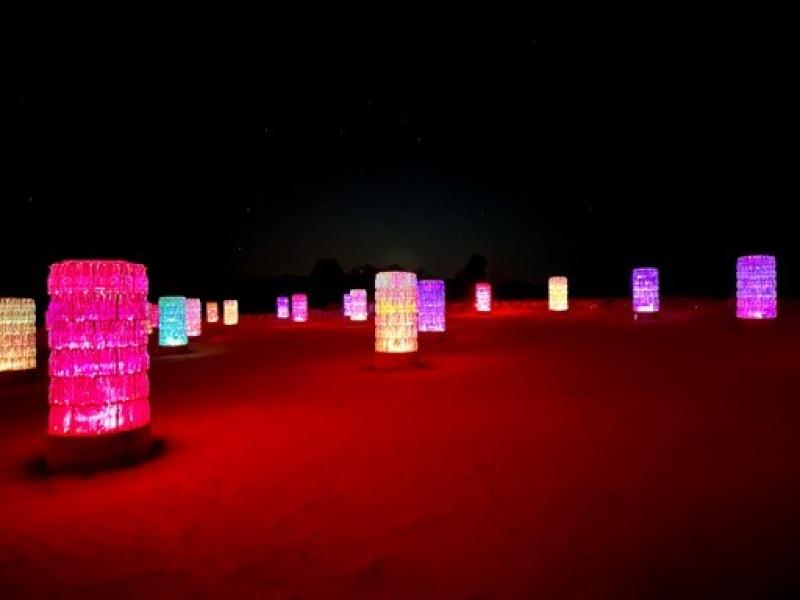 Bunte, zylindrische Leuchten auf rotem Sand im Dunkeln, ideal f&uuml;r stimmungsvolle Hotelterrassen.
