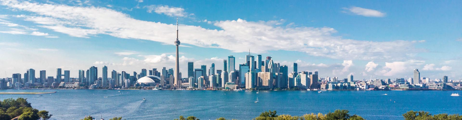 Skyline von Toronto mit hoch aufragenden Gebäuden, blauen Himmel und Wasser im Vordergrund.