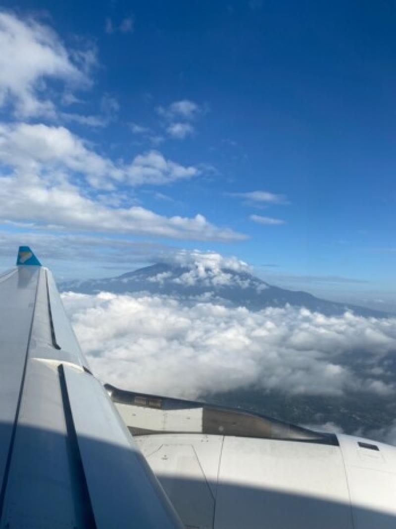 Blick aus dem Flugzeug auf Wolken, Berggipfel und blauen Himmel w&auml;hrend des Urlaubsflugs.
