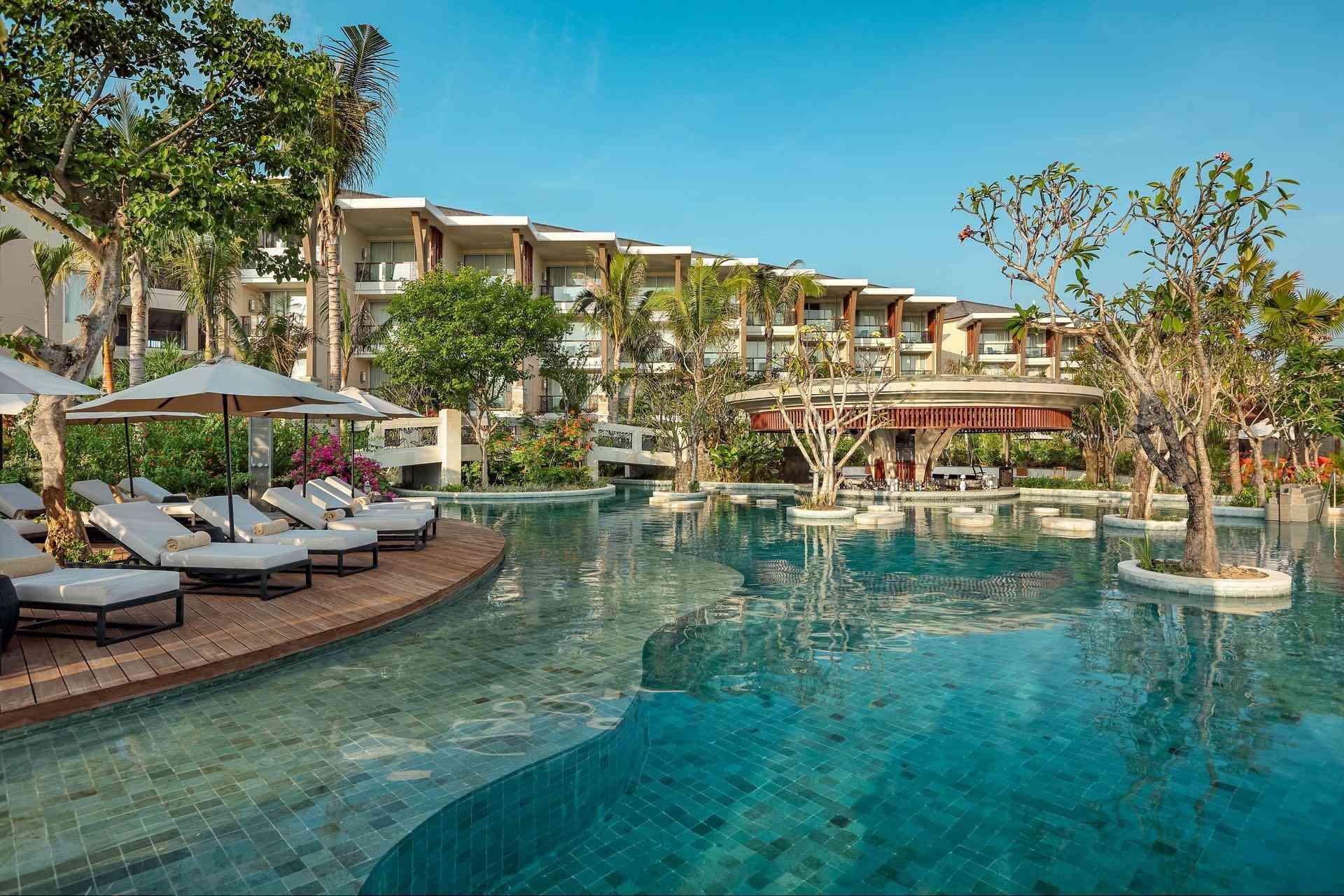 Luxuriöses Hotel mit großem Pool, Liegestühlen, Palmen und klarem blauem Himmel.